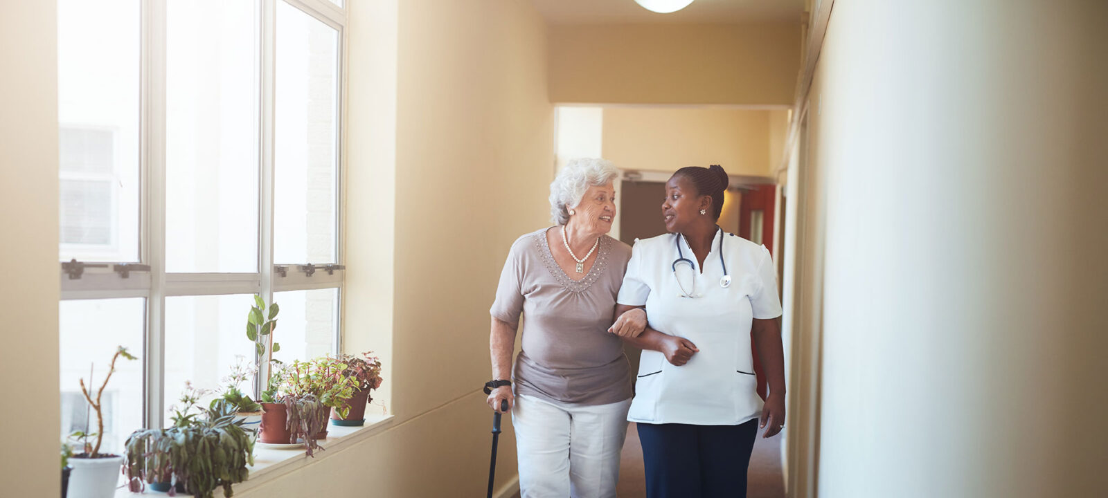 elderly woman and nurse walking arm and arm down hallway